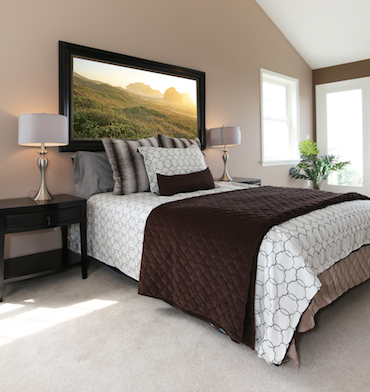 a carpeted room with a high sloping ceiling, two small bright windows, and a two perso bed with a bedside table and lamp on each side.