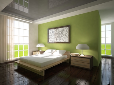 room with a hardwood floor bright windows on two sides and a two person bed with a bedside table and lamp on each side